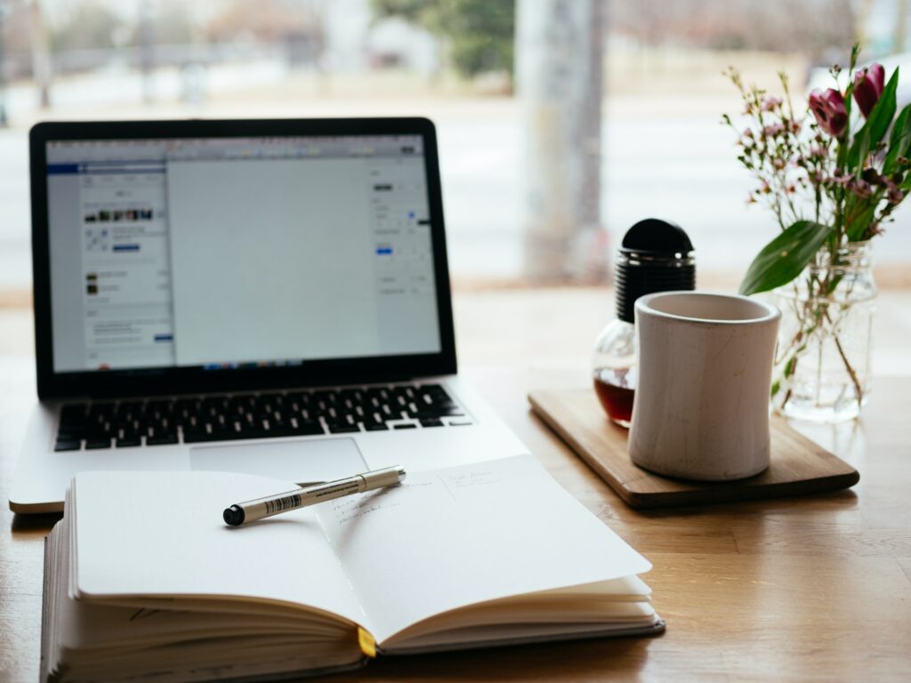 A laptop with an open notebook in front of it