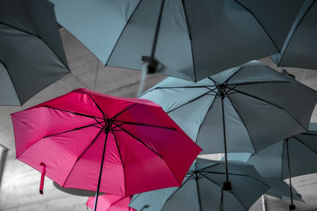 A colorful umbrella amongst gray ones